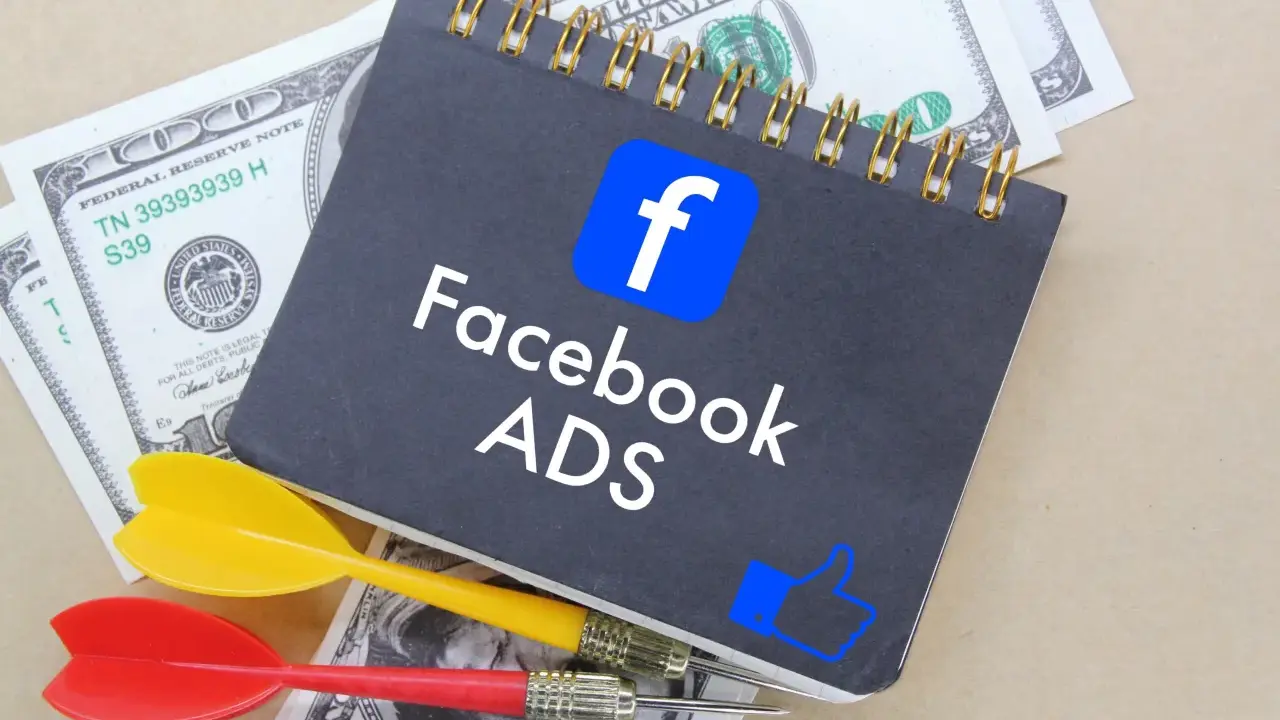 Notatnik z logo Facebook i napisem "Facebook ADS" leży na banknotach dolarowych. Obok znajdują się rzutki, symbolizujące celne reklamy mobilne.