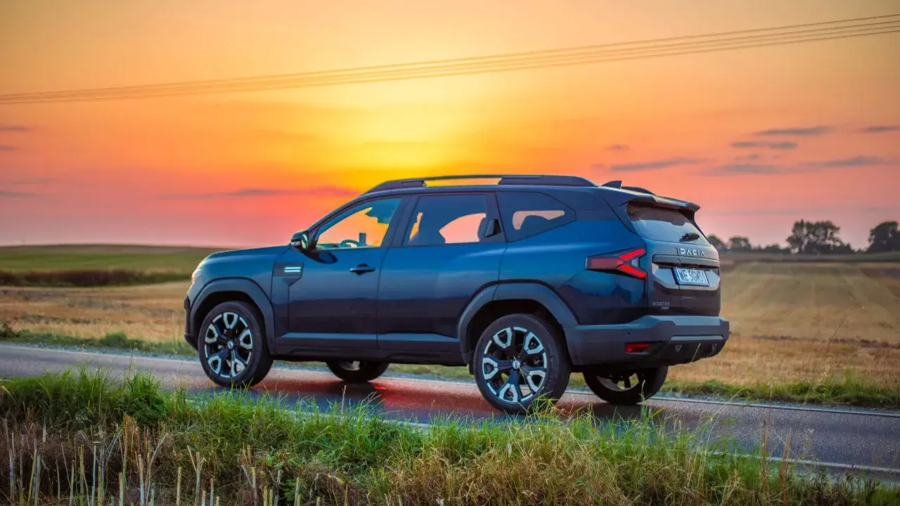 Ciemnoniebieski Dacia Bigster 2025 na tle zachodzącego słońca, na wiejskiej drodze.