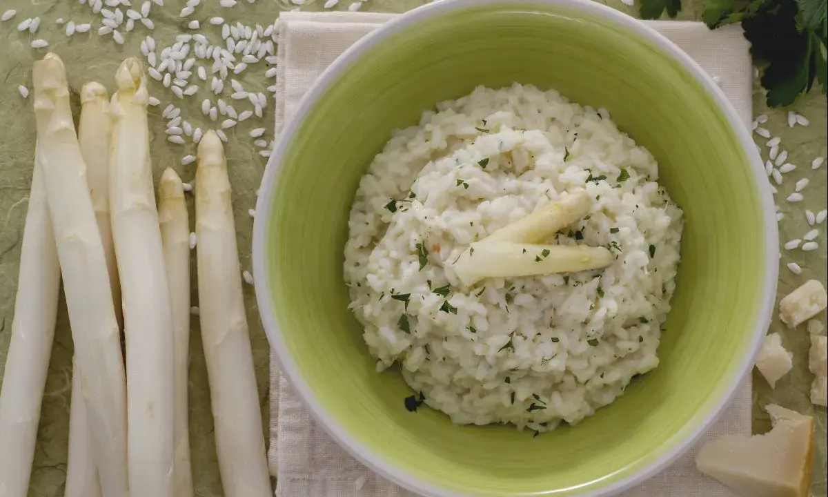 Delicioso risotto de espárragos cremoso, adornado con espárragos blancos y perejil picado. Acompañado de espárragos frescos y trozos de queso parmesano.