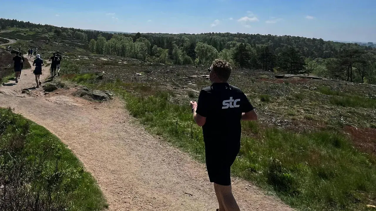 Grupp löpare njuter av trail running i en kuperad, skogig terräng under en solig dag.