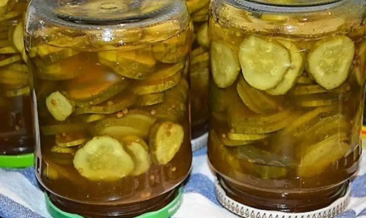 Słoiki pełne plasterków ogórków w zalewie z przyprawami, gotowe do podania jako dodatek do dań. Te ogórki w curry to smak lata zamknięty w słoiku.