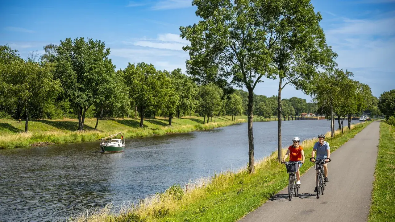 Zwei Radfahrer genießen eine Tour auf dem Dortmund-Ems-Kanal-Radweg. Ein kleines Boot fährt auf dem Wasser.