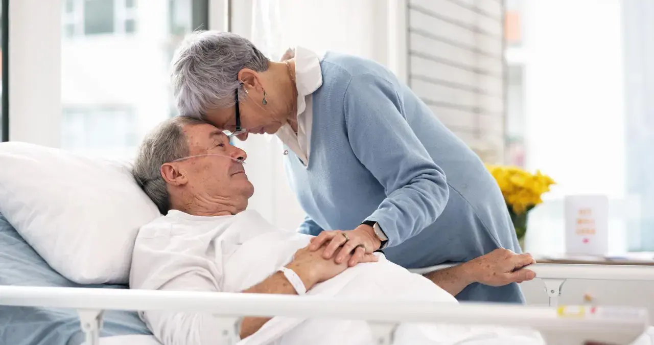 Czule pożegnanie. Kobieta pochyla się nad umierającym mężem, jak poznać że chory na alzheimera umiera, widać troskę i miłość.