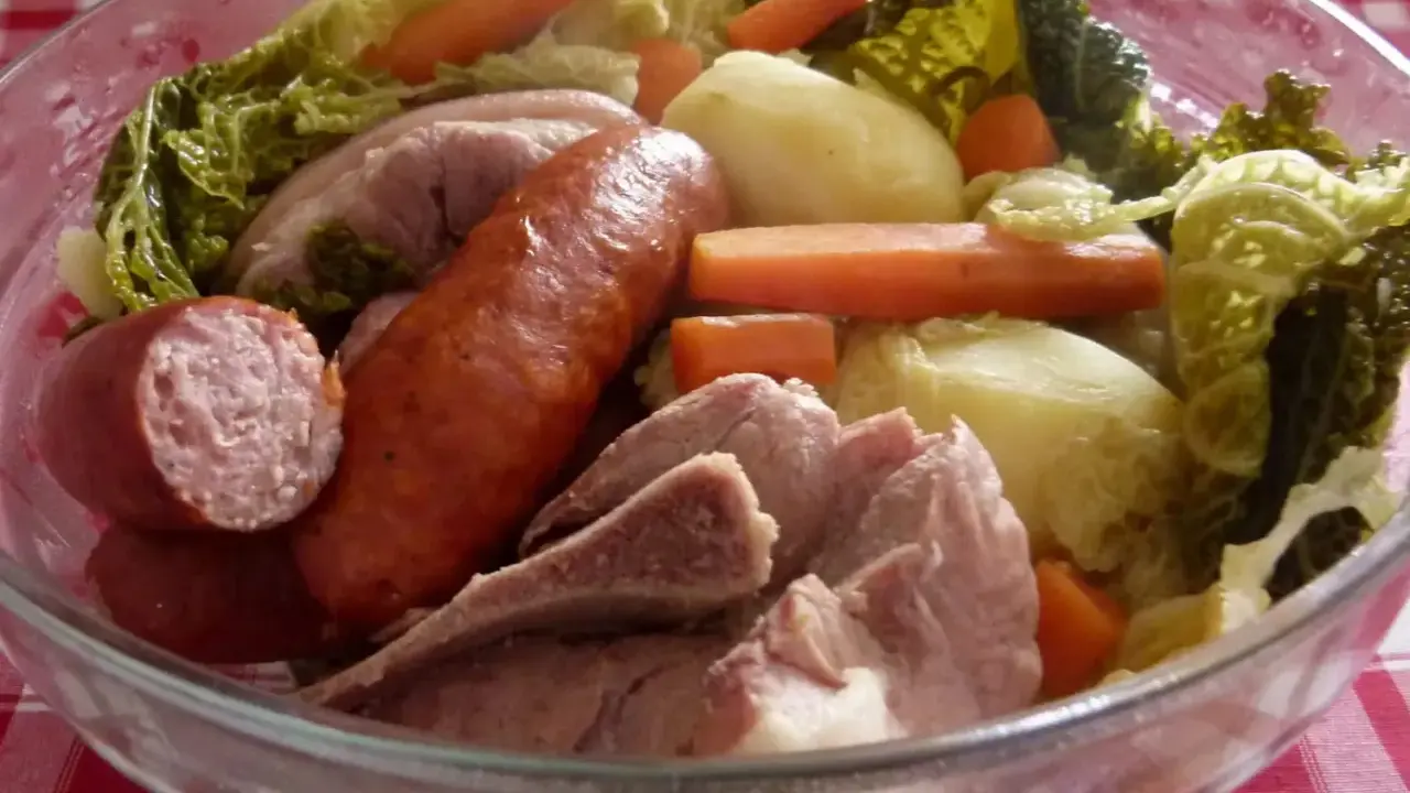 Un plat typique auvergnat : saucisses, porc, pommes de terre, carottes et chou savoyard mijotés dans un grand bol en verre.