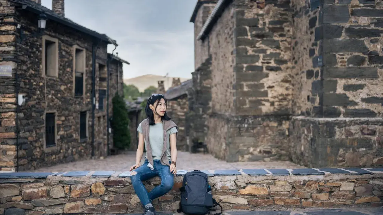 Junge Frau sitzt auf Steinmauer in historischem Dorf in Guadalajara, Spanien.