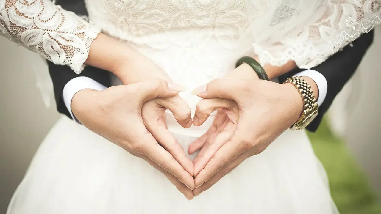 Manos formando un corazón, celebrando 2 años de casados. Vestido de novia blanco y traje negro.