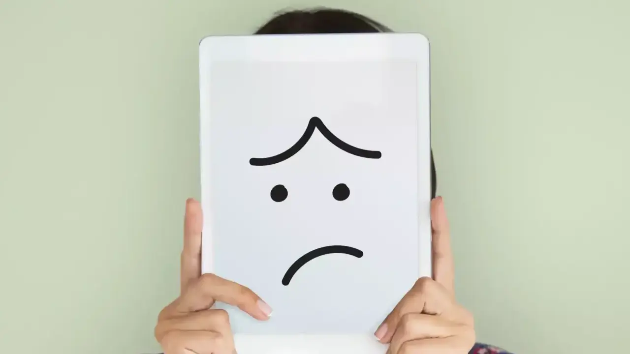 Una persona nasconde il volto dietro un tablet con un'espressione triste disegnata. La famiglia invischiata Minuchin potrebbe sentirsi così.