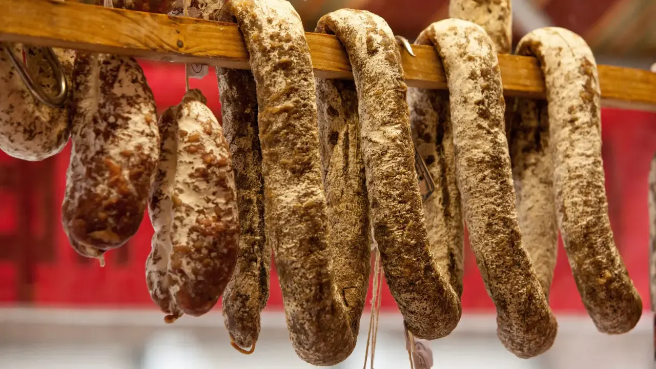Saucissons secs, une spécialité culinaire auvergnate, pendent sur un support en bois.