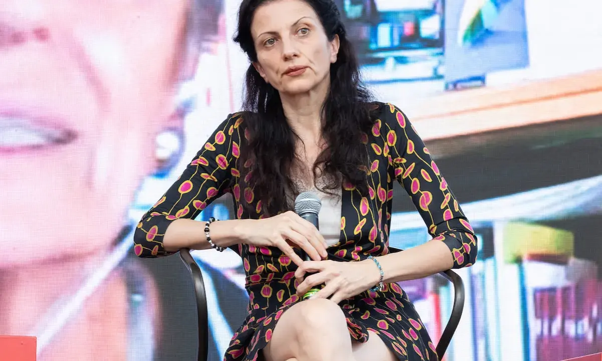 Veronica Tomassini, la cui età non è specificata, con un microfono in mano, indossa una giacca con fantasia floreale.