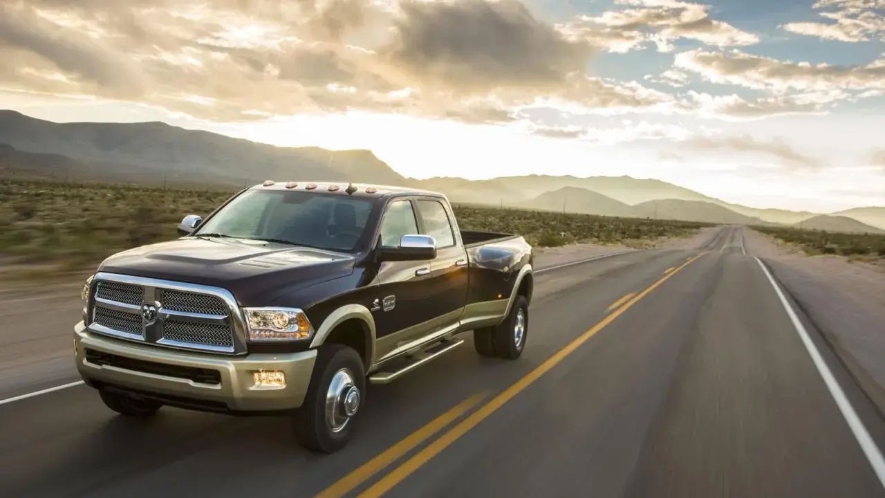 Ciemnobrązowy Dodge Ram 2500 z dwoma rzędami kół jedzie pustynną drogą o zachodzie słońca.
