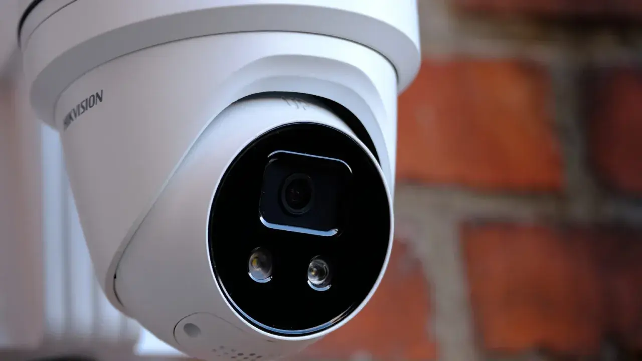 Vit övervakningskamera med Hikvision-logotyp, monterad mot en tegelvägg. Ger trygghet med larmklass 1.