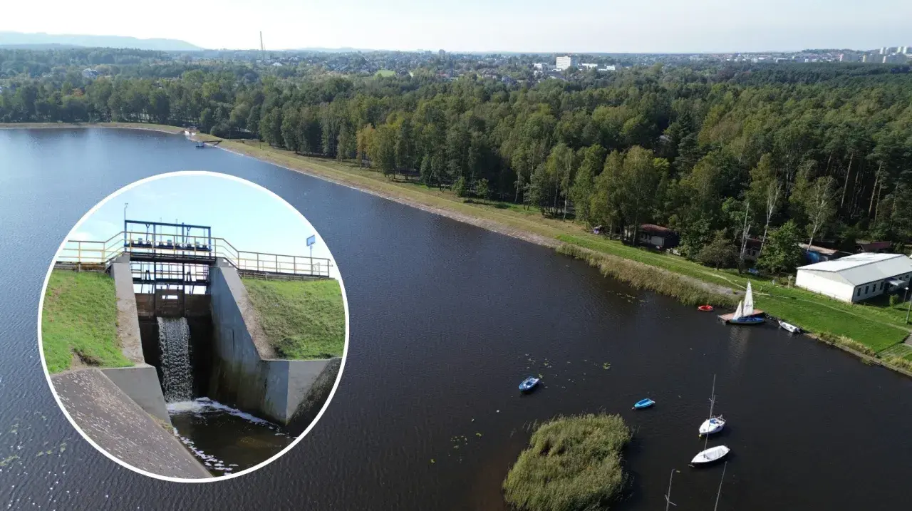 Widok na zbiornik wodny z zaporą i spływającą wodą. Na wodzie kilka łodzi, w tle las i zabudowania. To piękne **chechło** jest idealnym miejscem do wypoczynku.