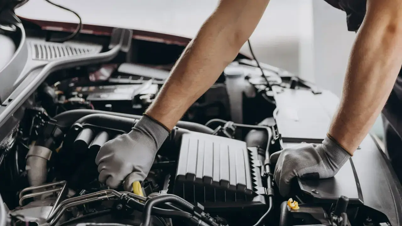 Mechanik w rękawiczkach pracuje przy silniku, dbając o zgodność z normami emisji spalin i tabelą CO2.