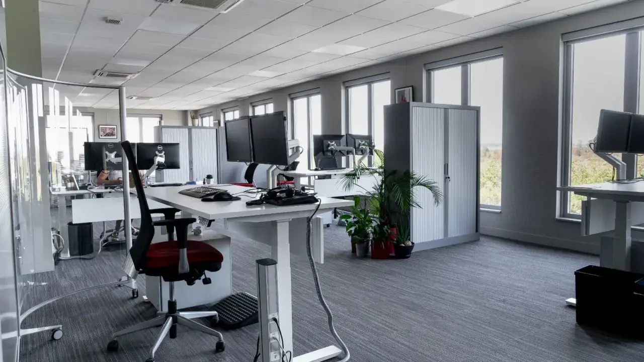 Aménagement moderne de bureaux en open space avec postes de travail équipés de plusieurs écrans, chaises ergonomiques et rangements.