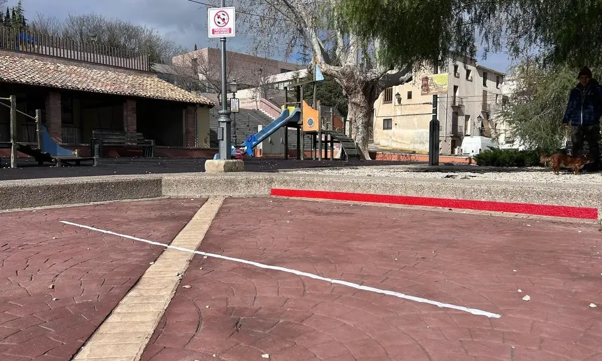 Un parque infantil con toboganes y columpios, evocando los **juegos de antes en la calle**. Un hombre pasea a su perro.