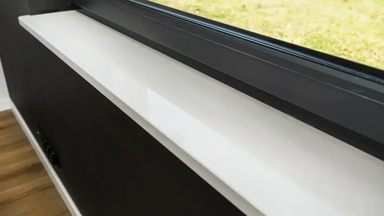 Biały, lśniący parapet z konglomeratu, idealnie wypolerowany, stanowi eleganckie wykończenie okna.