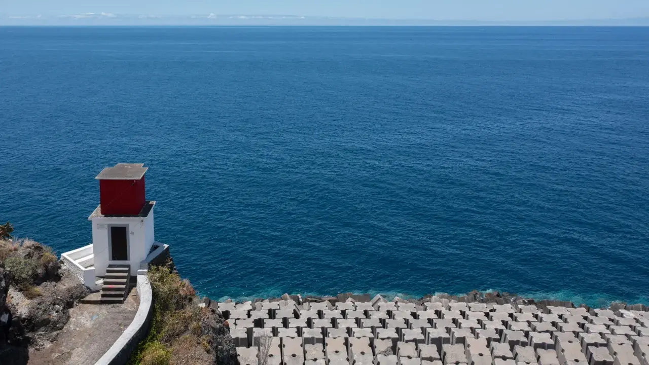 Kleines rotes Haus auf Felsen am Meer bei Ribeira Brava. Wellenbrecher aus Beton säumen die Küste.
