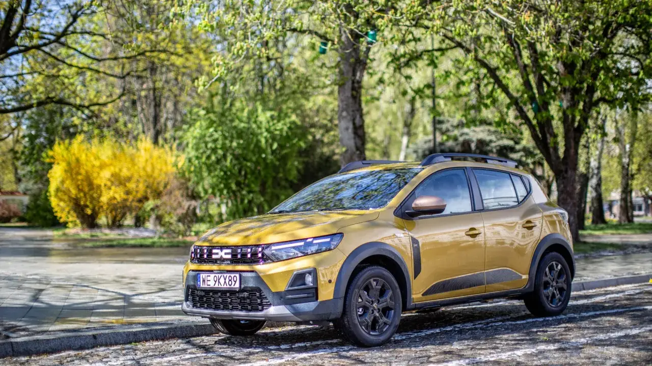 Złoty Dacia Sandero Stepway na tle wiosennej zieleni i kwitnącego krzewu.