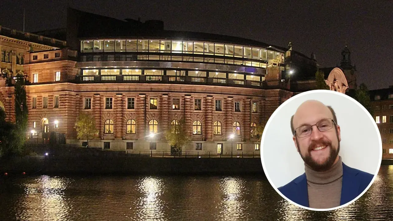 En man ler mot kameran framför Riksdagshuset i Stockholm, en symbol för representativ demokrati.