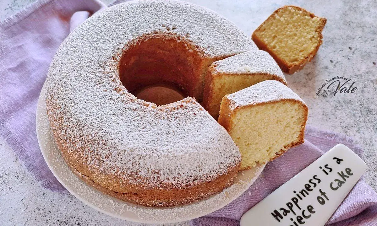 Un ciambellone soffice come una nuvola, cosparso di zucchero a velo, con fette tagliate pronte da gustare.