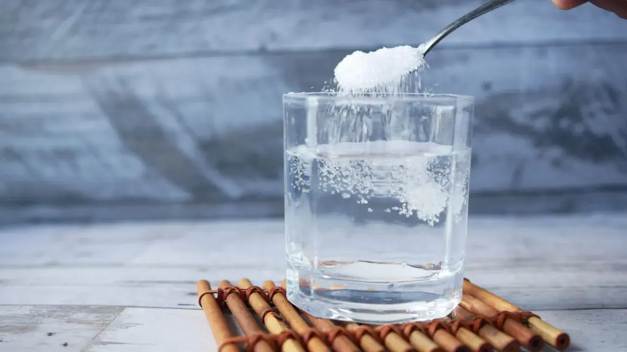 Salz und Zucker werden in ein Glas Wasser gegeben, um Elektrolyte selber machen.