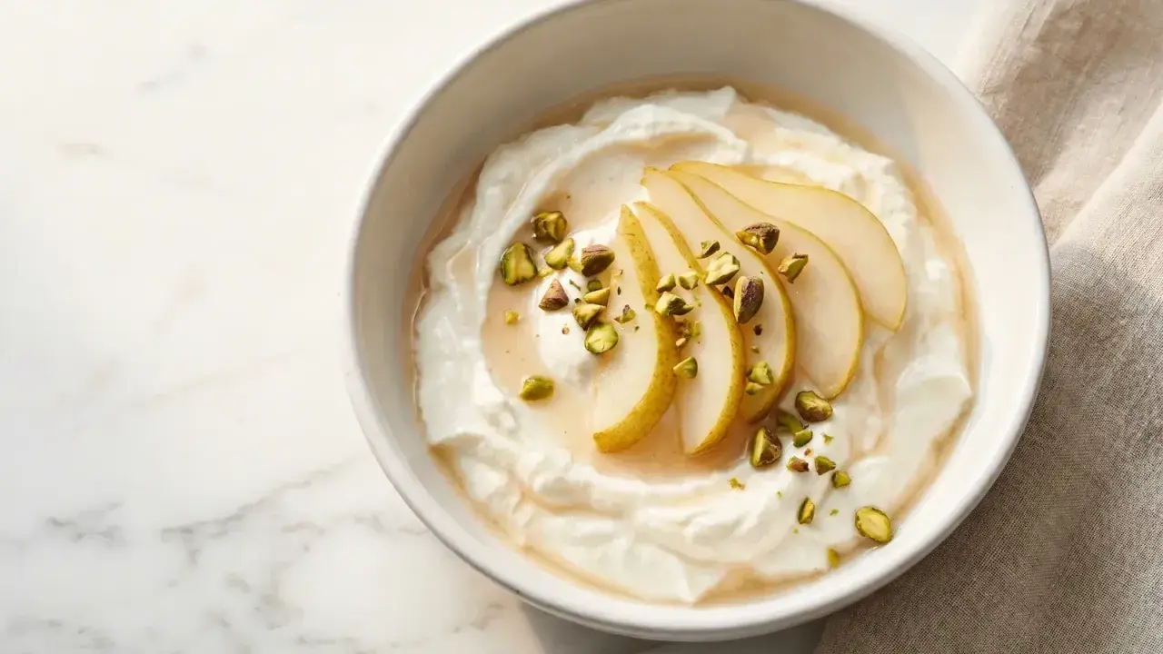 Cremiger Joghurt, der zu lange im Joghurtbereiter war, serviert mit Birnenspalten, Honig und gehackten Pistazien.