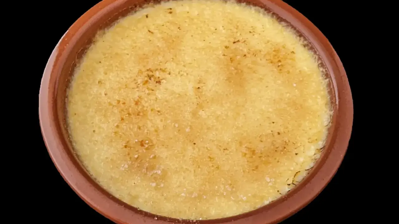 Crème brûlée dans un ramequin en terre cuite, sa surface caramélisée craque sous la cuillère.