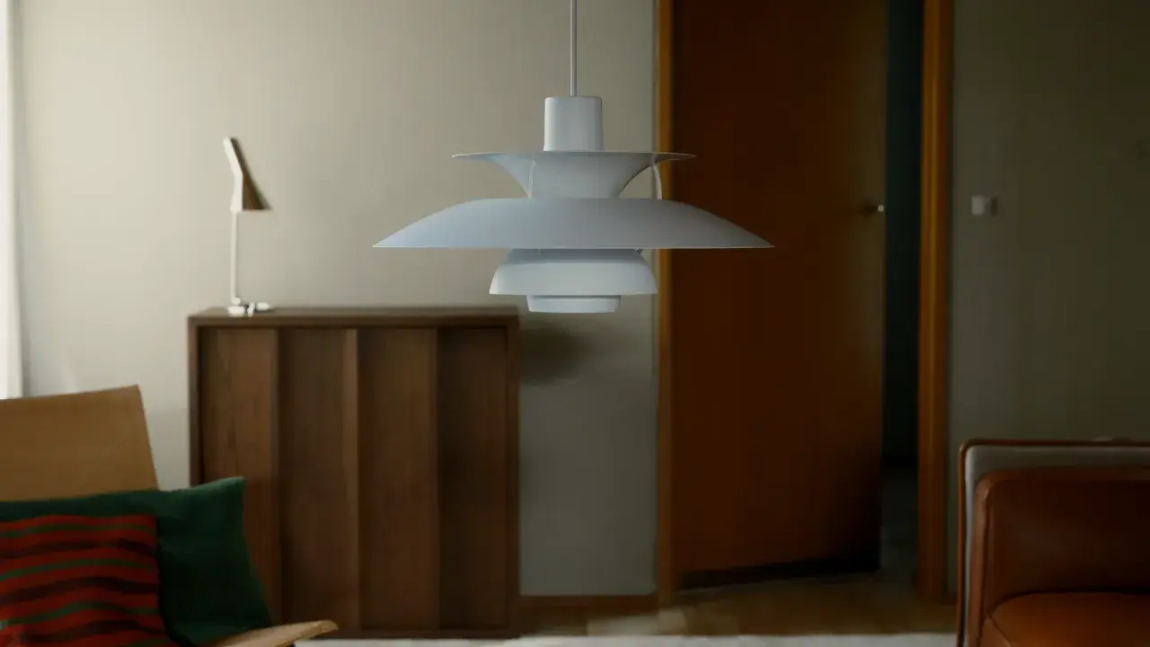 En ikonisk PH-lampa från Poul Henningsen hänger över ett vardagsrum med en läderfåtölj och en träbyrå.