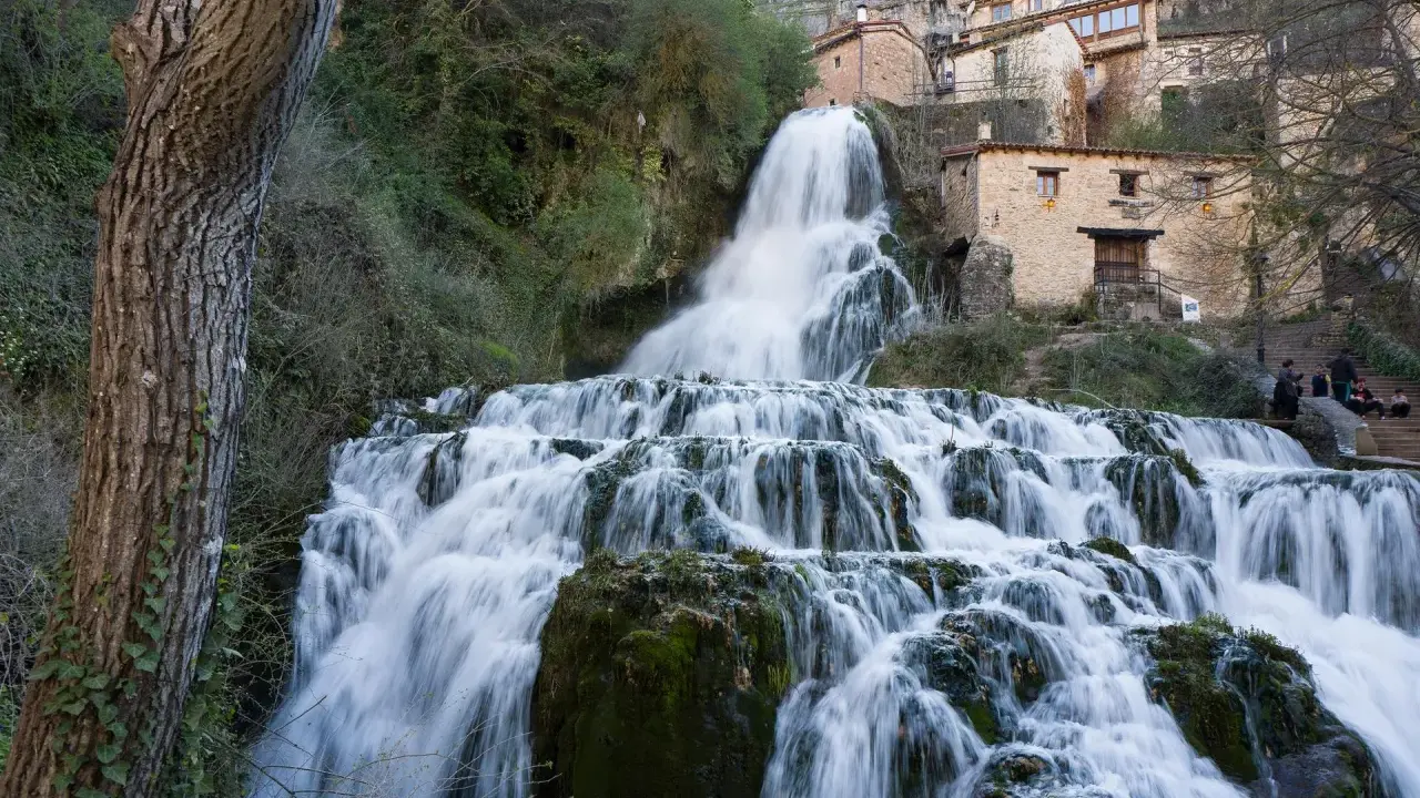 Tosender Wasserfall stürzt über Felsen, Häuser von Orbaneja del Castillo schmiegen sich an den Hang.