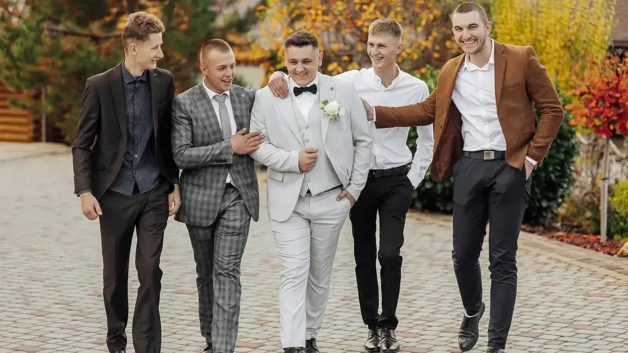 Pięciu panów w garniturach, idealnie dobranych na ślub. Pan młody w jasnym, koledzy w ciemniejszych stylizacjach.