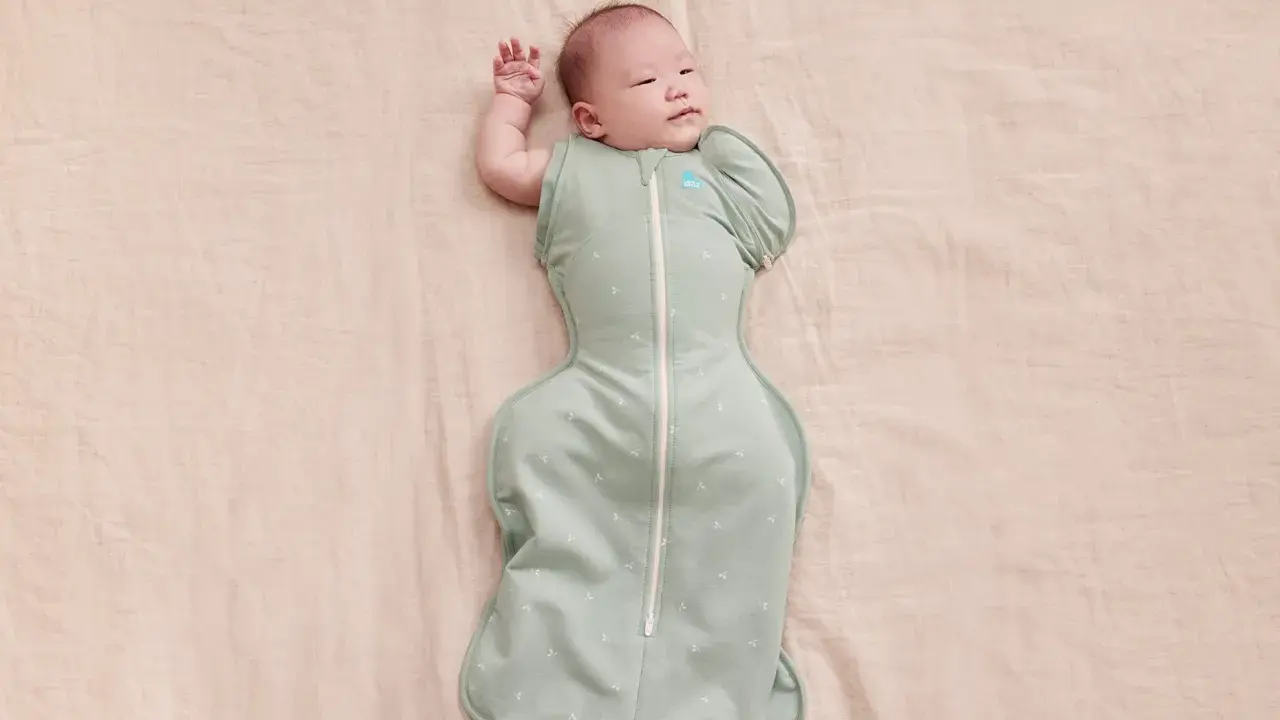Un neonato dorme sereno, avvolto in una fascia che lo culla dolcemente.