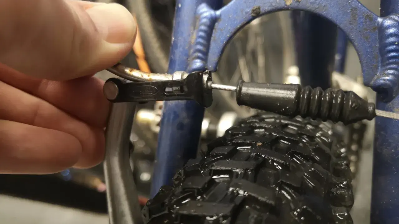 Dłoń reguluje linkę hamulca v-brake, by wyeliminować piszczące hamulce w rowerze.