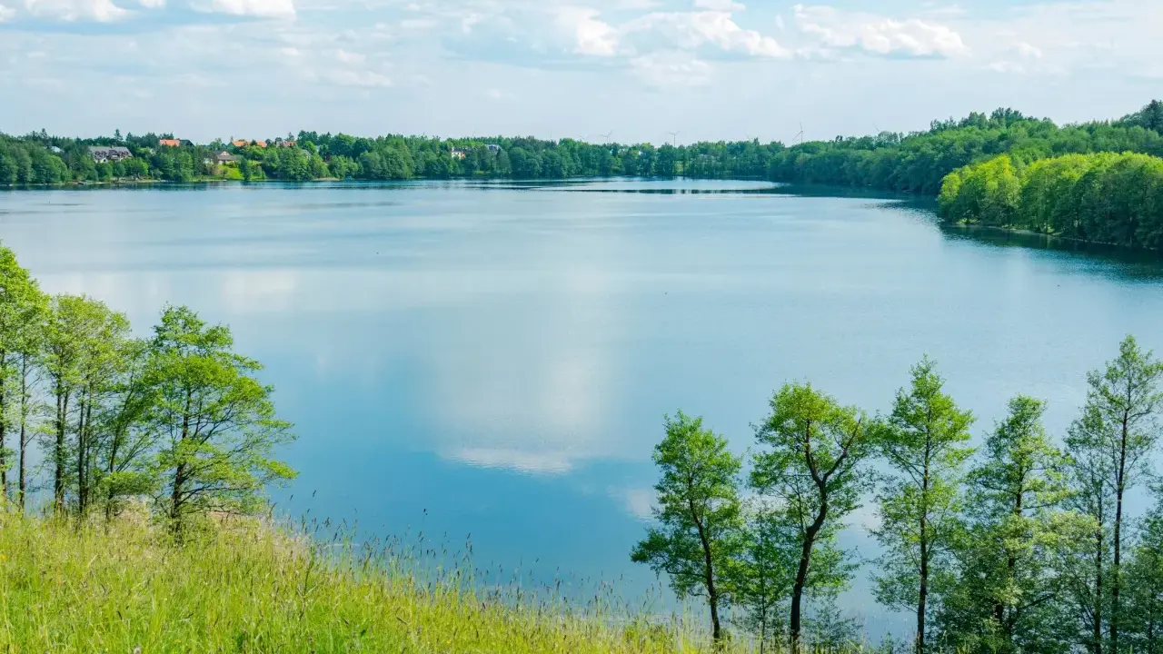 Malownicze żnin jezioro otoczone zielenią, z widocznymi domami na horyzoncie i błękitnym niebem z chmurami.