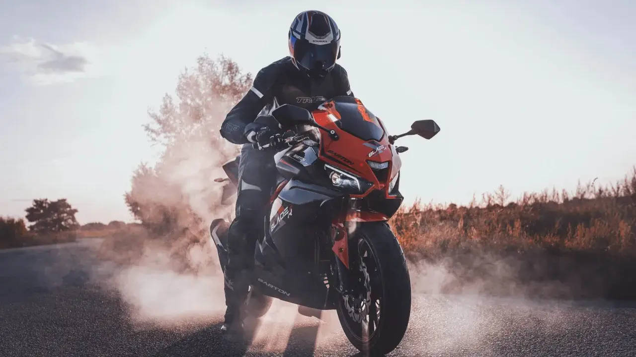 Motocyklista w kasku i kombinezonie na sportowym motocyklu, otoczony dymem. Czy motorem można jeździć po autostradzie? Tak, jeśli spełnia określone wymogi.