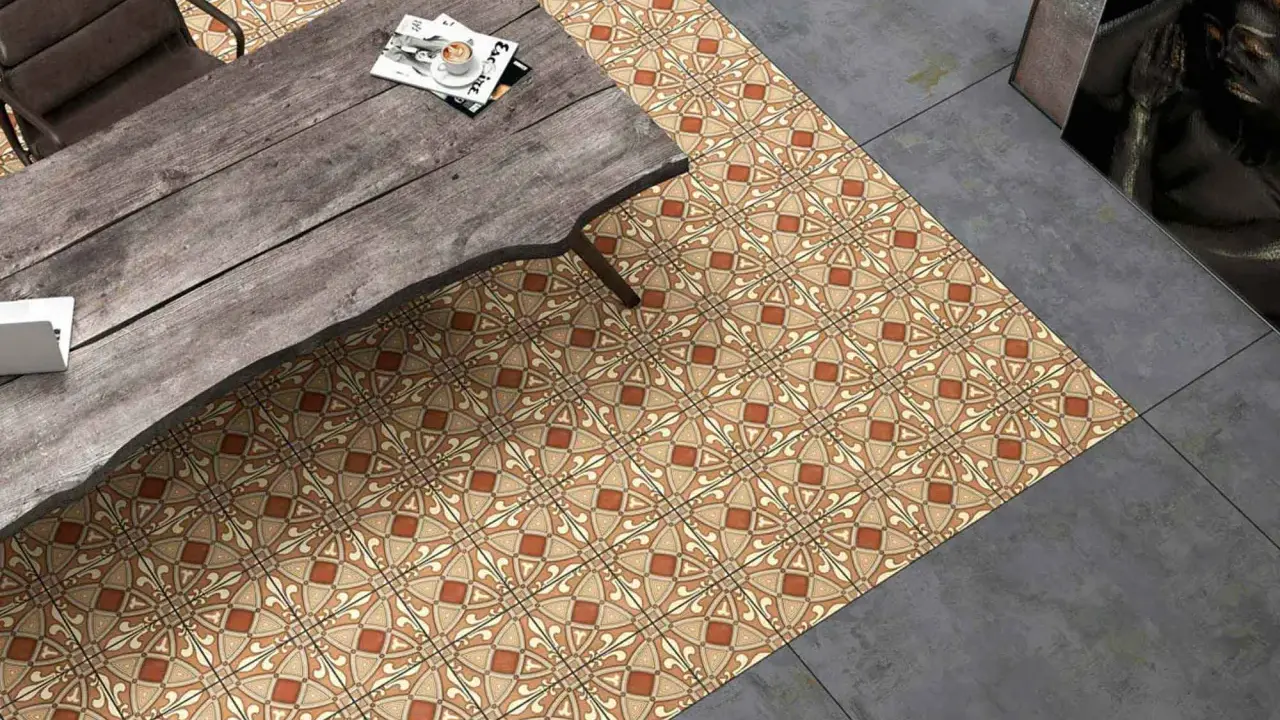 Un suelo hidráulico con diseño geométrico en tonos tierra y ocre, junto a un suelo de cemento pulido. Una mesa de madera rústica y una silla completan la escena.