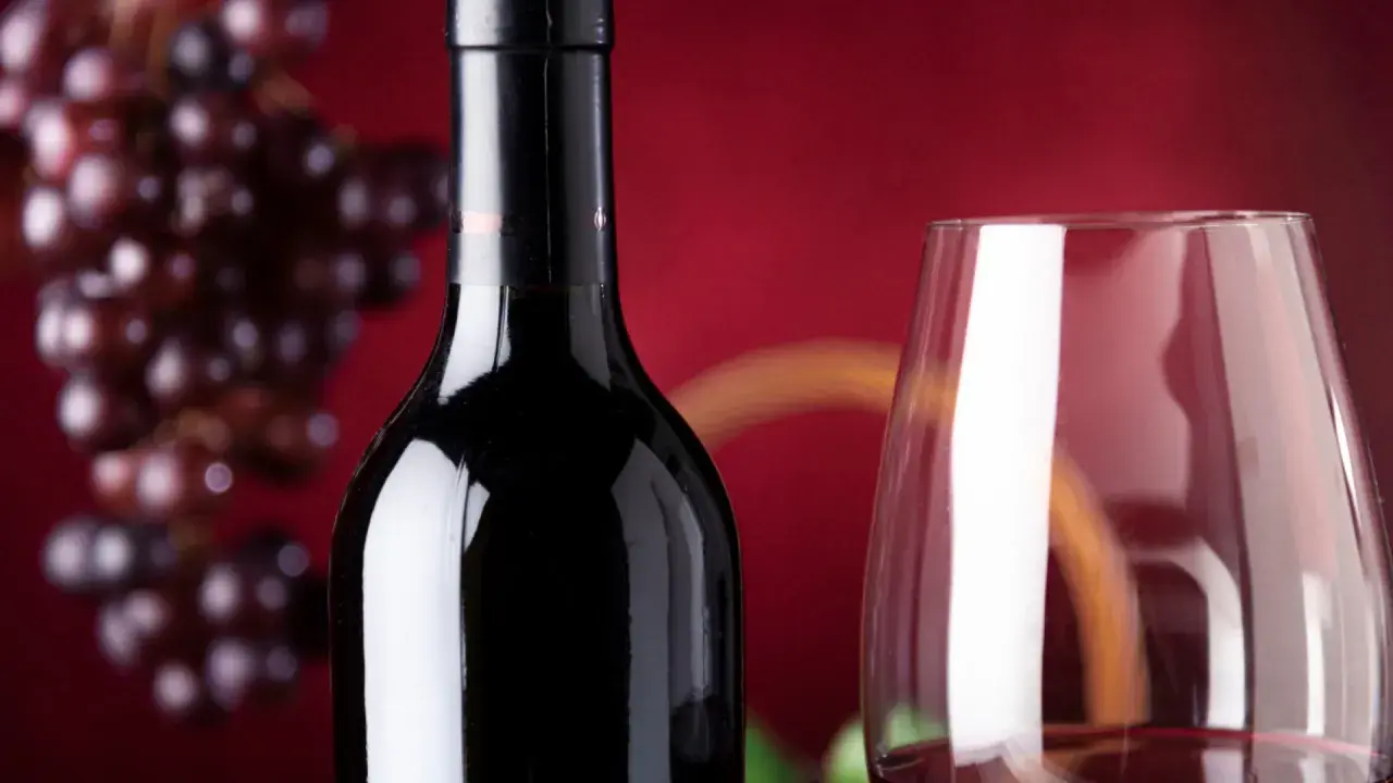 Bouteille de vin rouge connu, verre à vin et grappe de raisins sur fond rouge.