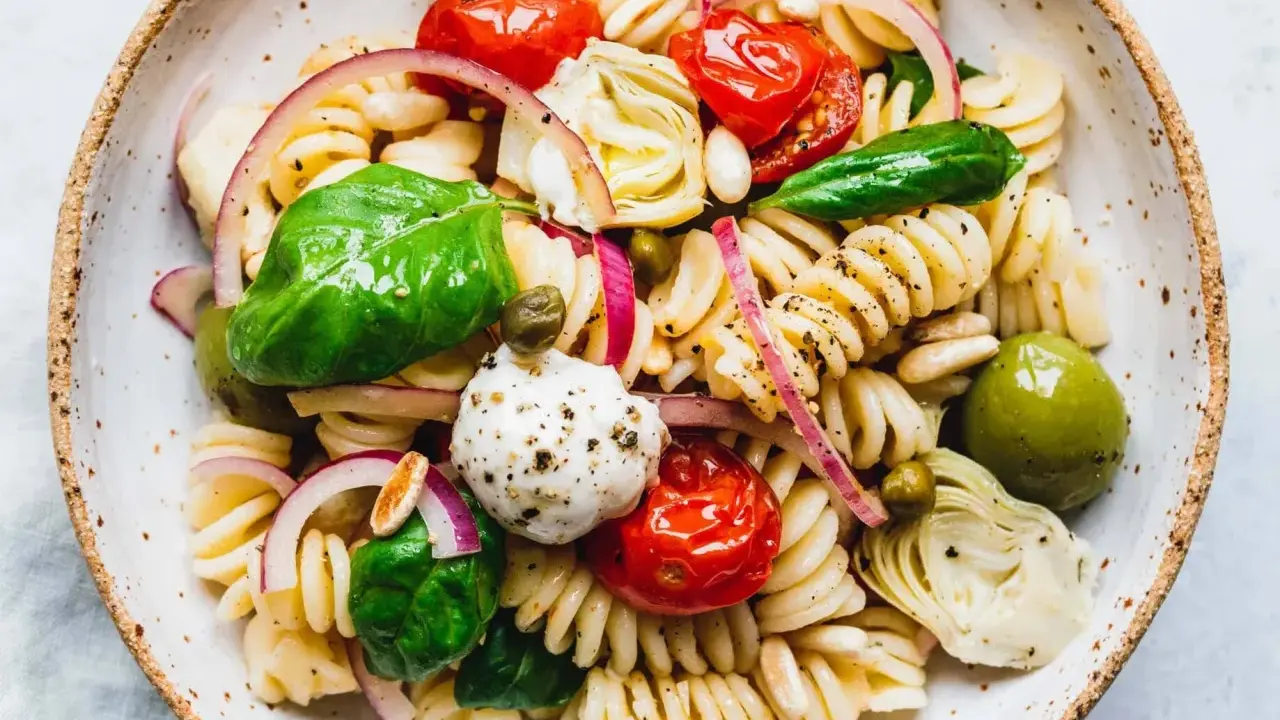 Ein bunter vegetarischer Nudelsalat mit Fusilli, Kirschtomaten, Mozzarella-Kugeln, Artischockenherzen, Oliven und frischem Basilikum.