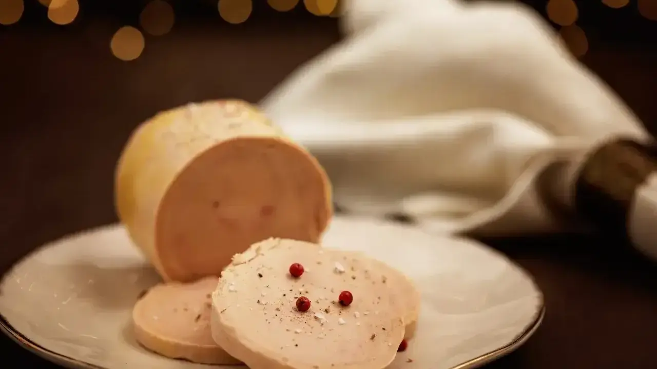 Tranche de foie gras, une des spécialités culinaires Dordogne, assaisonnée de poivre et de baies roses sur une assiette blanche.