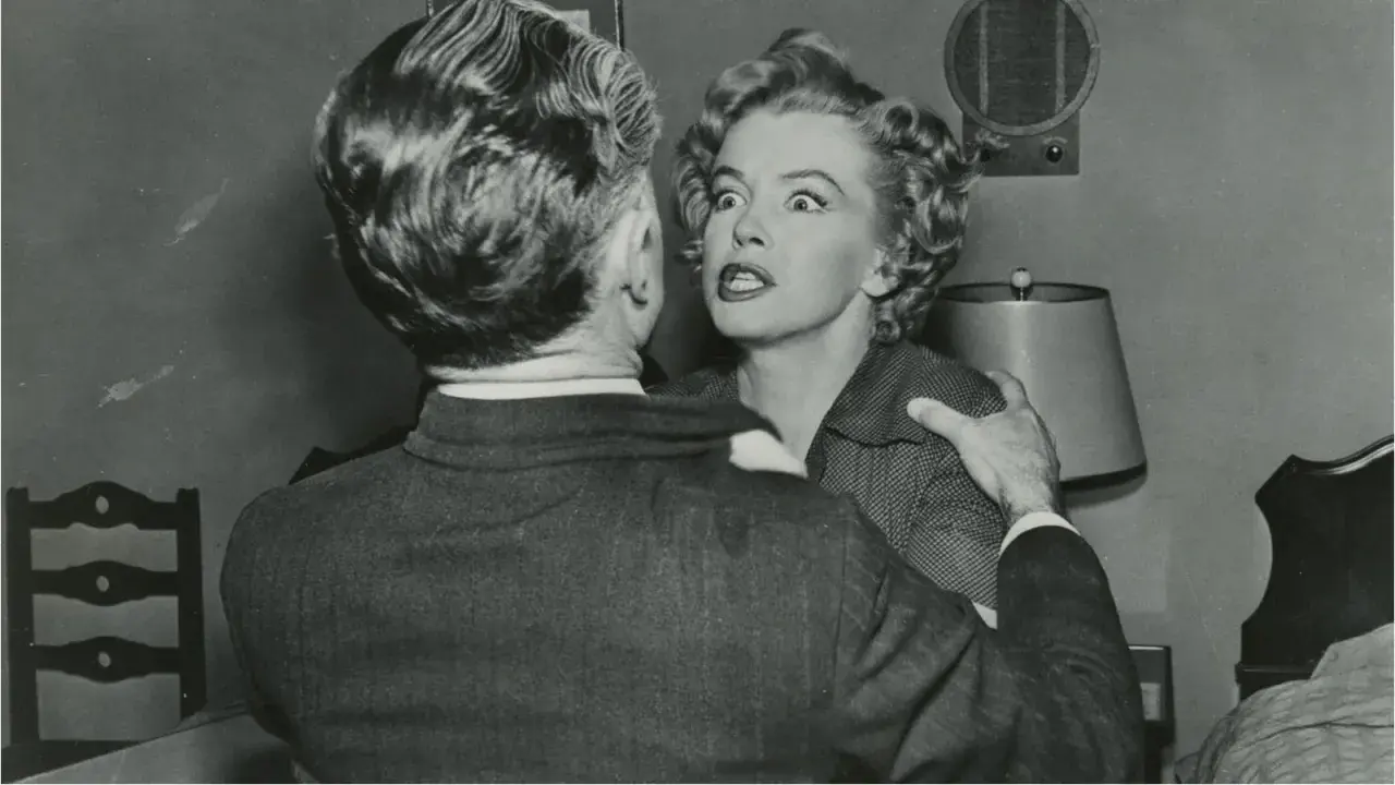 Marilyn Monroe med chockat uttryck i en scen från en av hennes filmer, hon håller fast vid en mans axel.