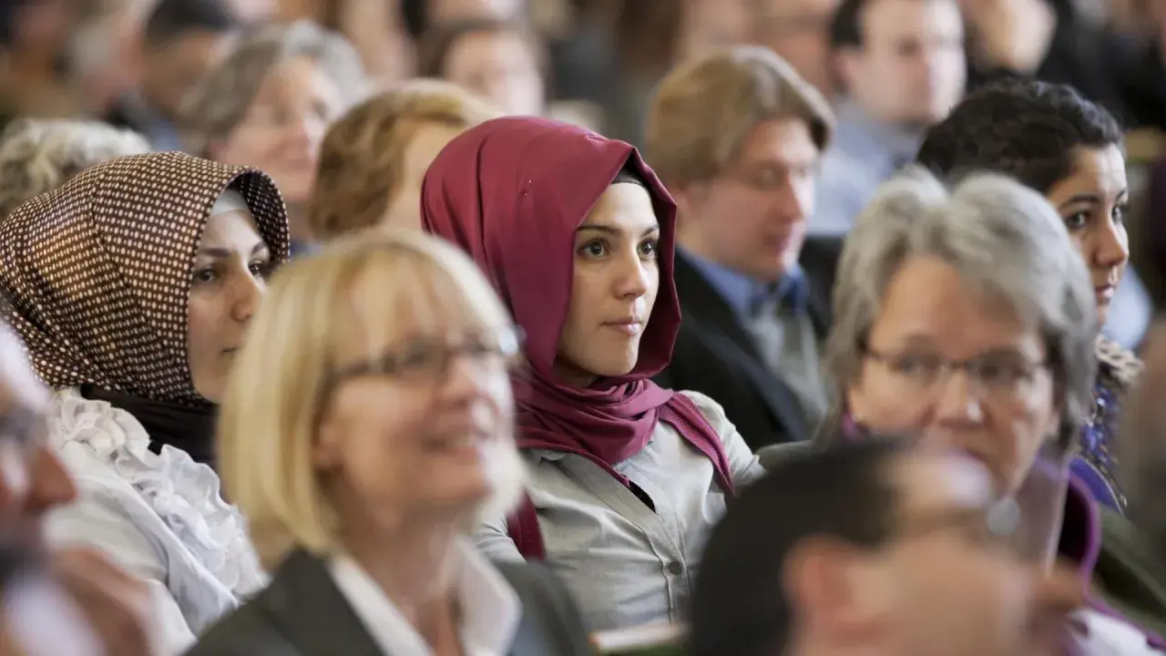 Junge Frau mit einem roten islamischen Kopftuch im Publikum.