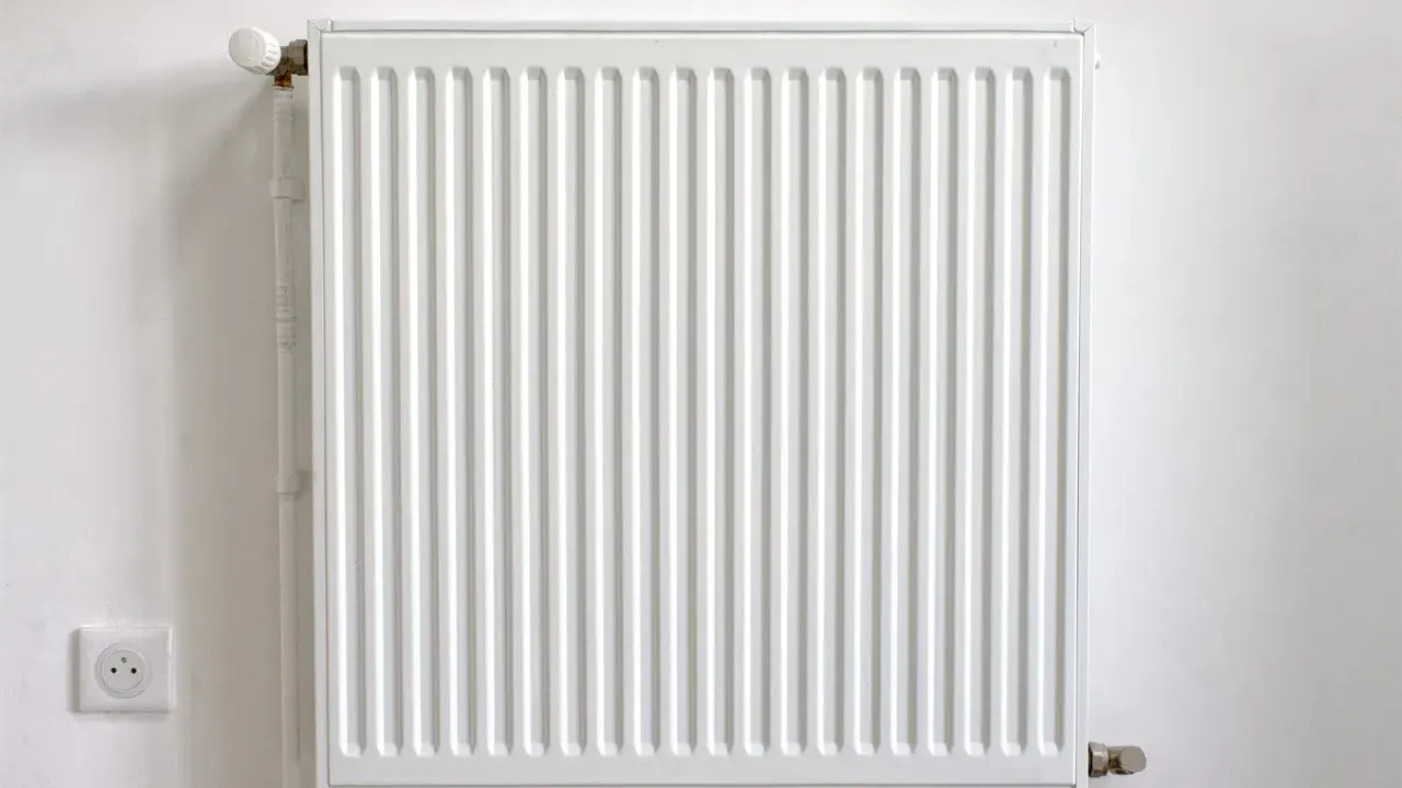 Radiador blanco con termostato, junto a un enchufe. Podría estar haciendo ruido radiador.