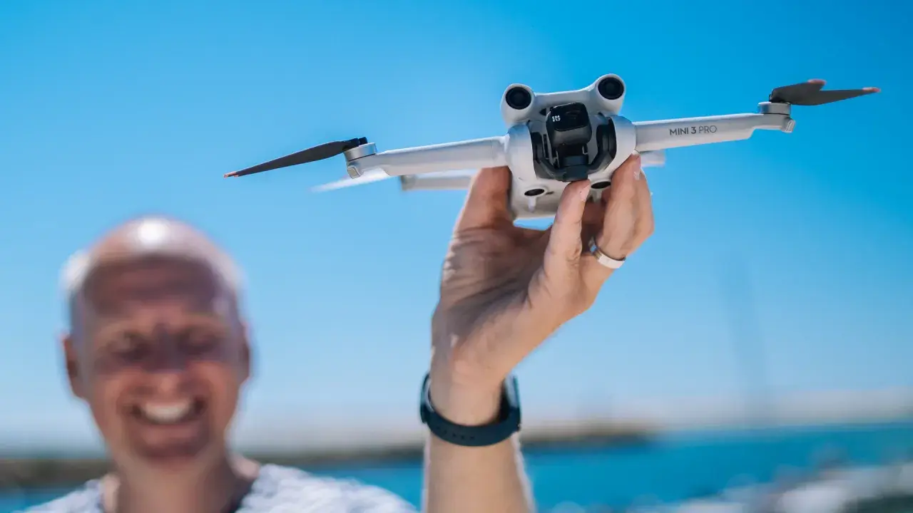 Ręka trzyma drona DJI Mini 3 Pro, gotowego do lotu. Jego imponujący zasięg pozwoli na uchwycenie niesamowitych ujęć.
