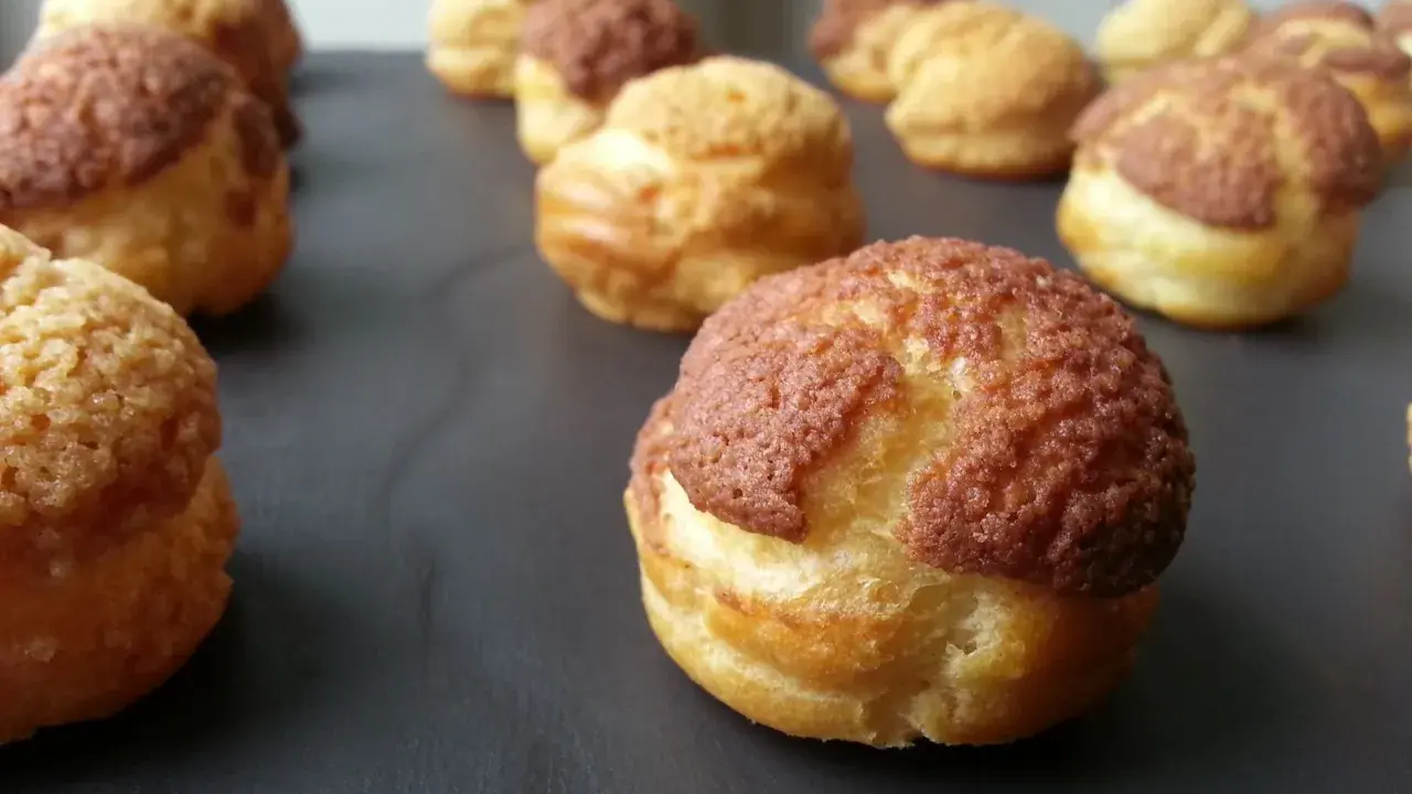 Une rangée de choux craquelins dorés et croustillants, certains avec un dessus brun, prêts à être dégustés.