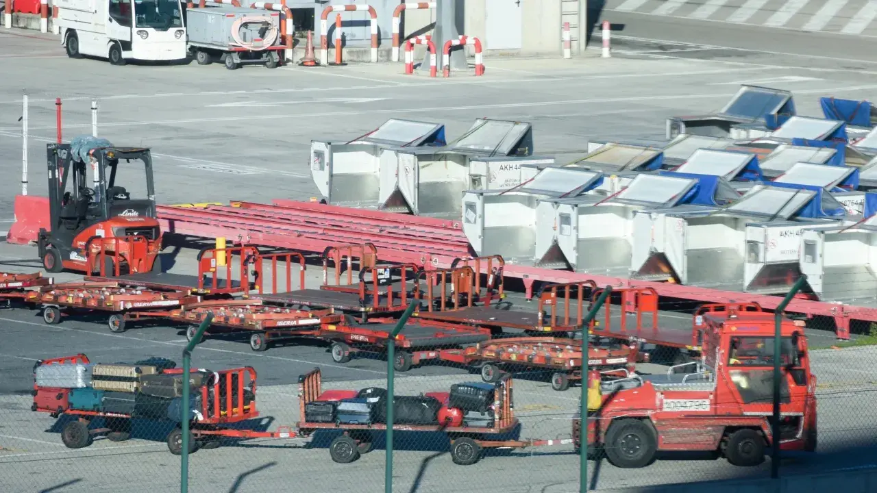 Röda lastbilar och vagnar med bagage på en solig yta vid teneriffa flygplats. En gaffeltruck står redo.