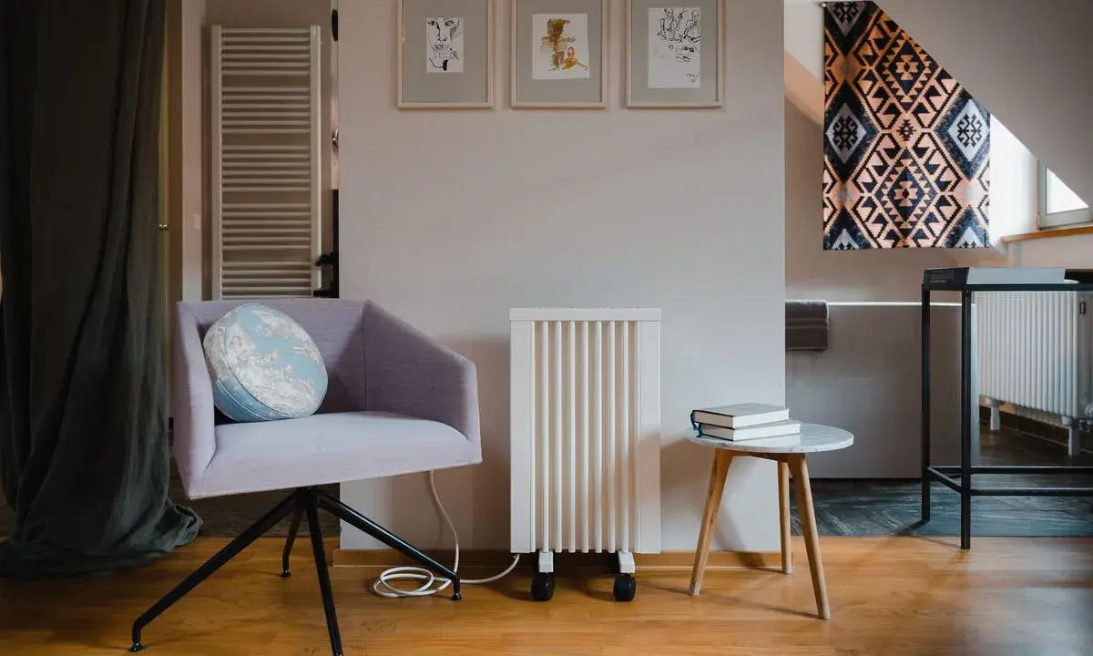 Un fauteuil confortable, un radiateur rayonnant blanc et une petite table avec des livres créent un coin lecture cosy.