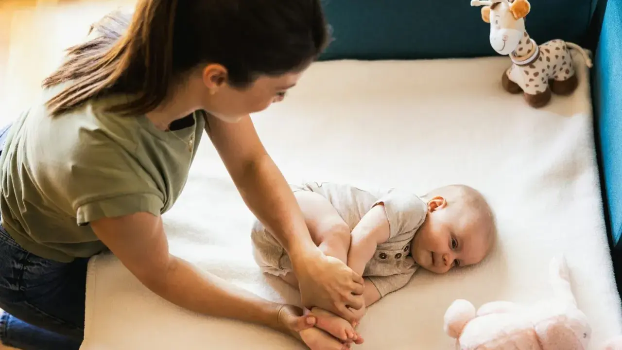 Mama bawi się z 3 miesięcznym dzieckiem, delikatnie masując jego stópki. Obok leżą pluszowe zabawki.