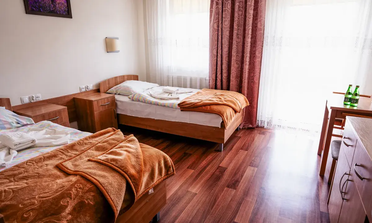 Pokój w sanatorium Busko-Zdrój, prywatnie Krystyna. Dwa łóżka, szafki nocne, stół z krzesłem i butelkami wody.