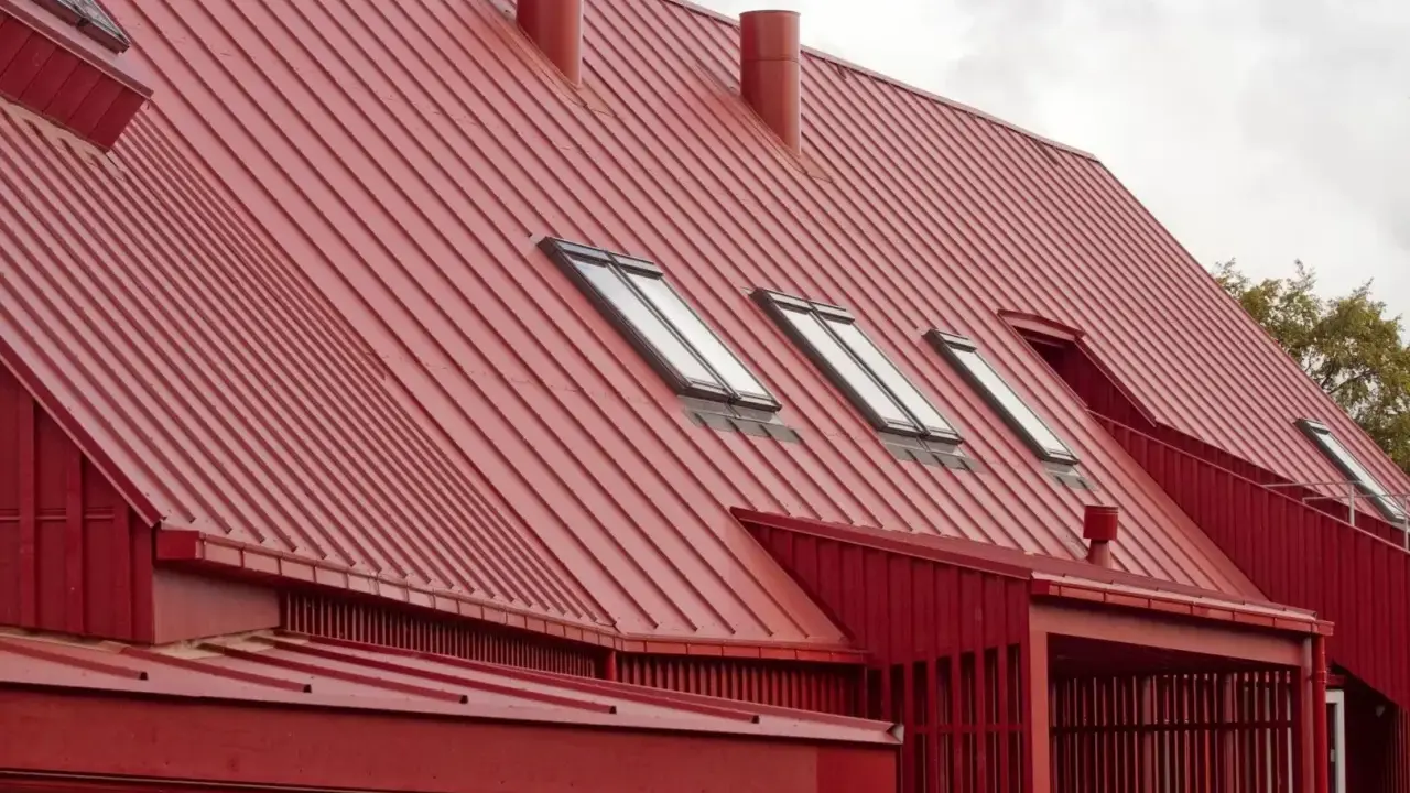 Rött, bandat plåttak med flera takfönster och skorstenar. Ett modernt hus med en slående takkonstruktion.