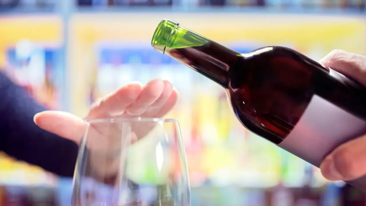 Hand stoppt Weinglas, während eine Flasche Rotwein eingegossen wird. Ein Symbol für bewussten Weinkonsum weltweit.