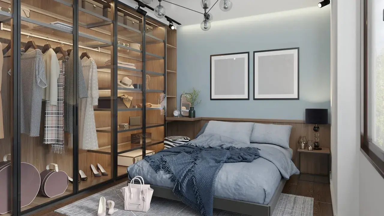 Chambre moderne avec dressing vitré bien organisé, lit bleu douillet et deux cadres vides au mur.